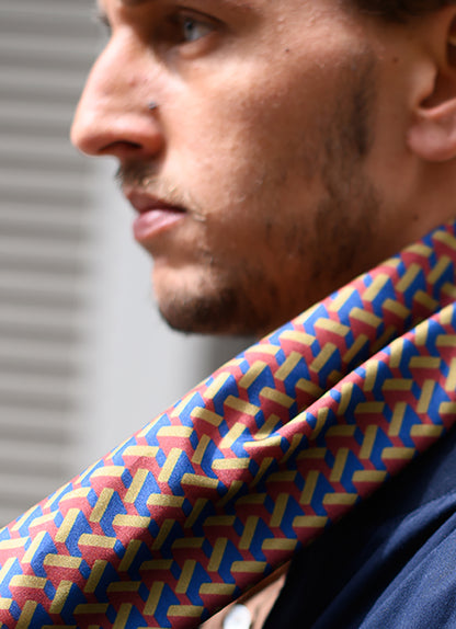 Foulard en soie 110 Meilleur Ami Paris, porté homme. Imprimé graphique effet 3D, coloris bordeaux, kaki et bleu, vue de profil.