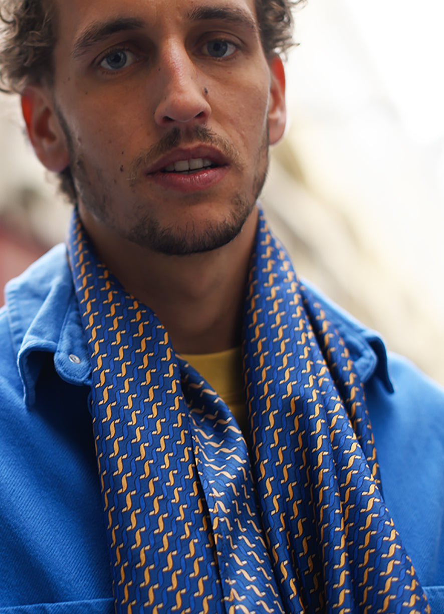 Foulard en soie 111 Meilleur Ami Paris, porté dénoué homme, imprimé bleu et ocre sur veste bleue.
