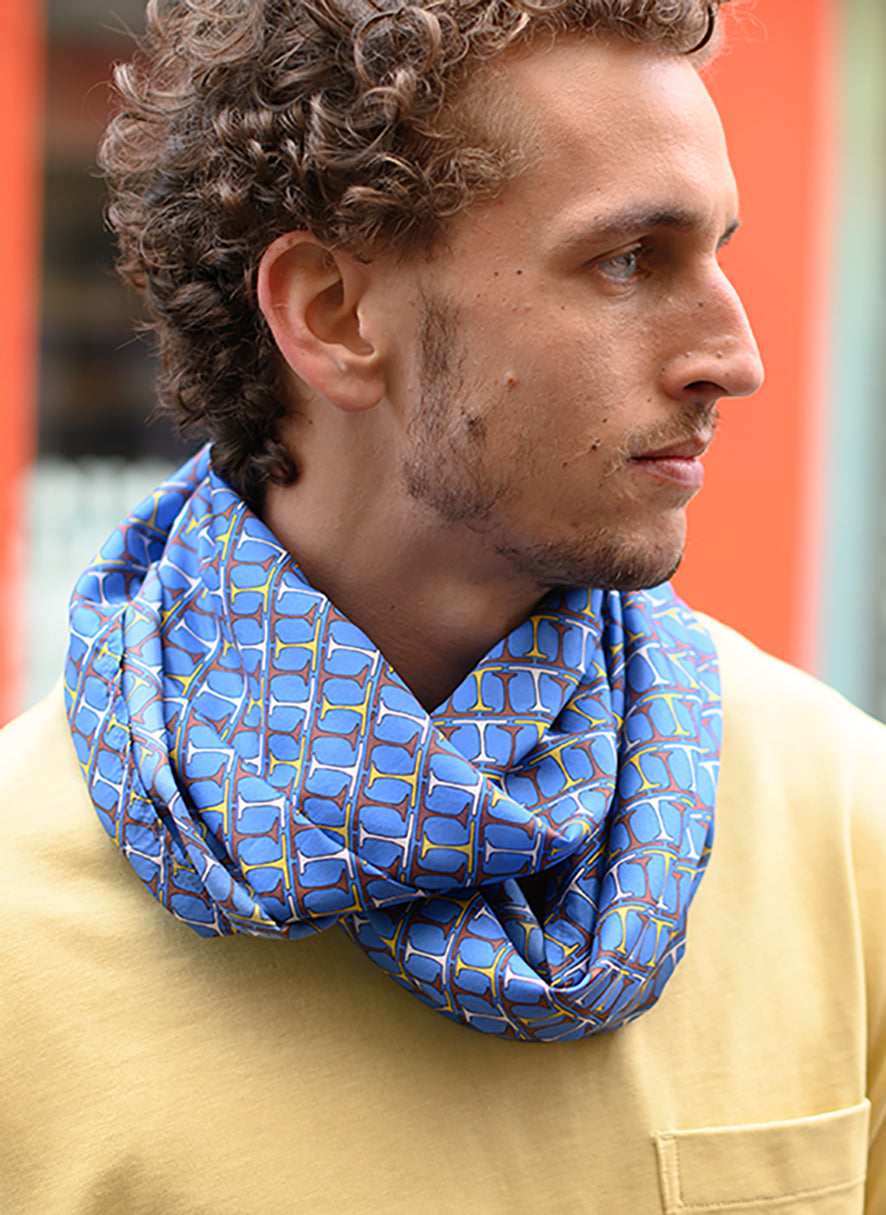 Foulard en soie 18 Meilleur Ami Paris, porté homme. Motifs bordeaux, blancs et jaunes sur fond bleu lumineux.