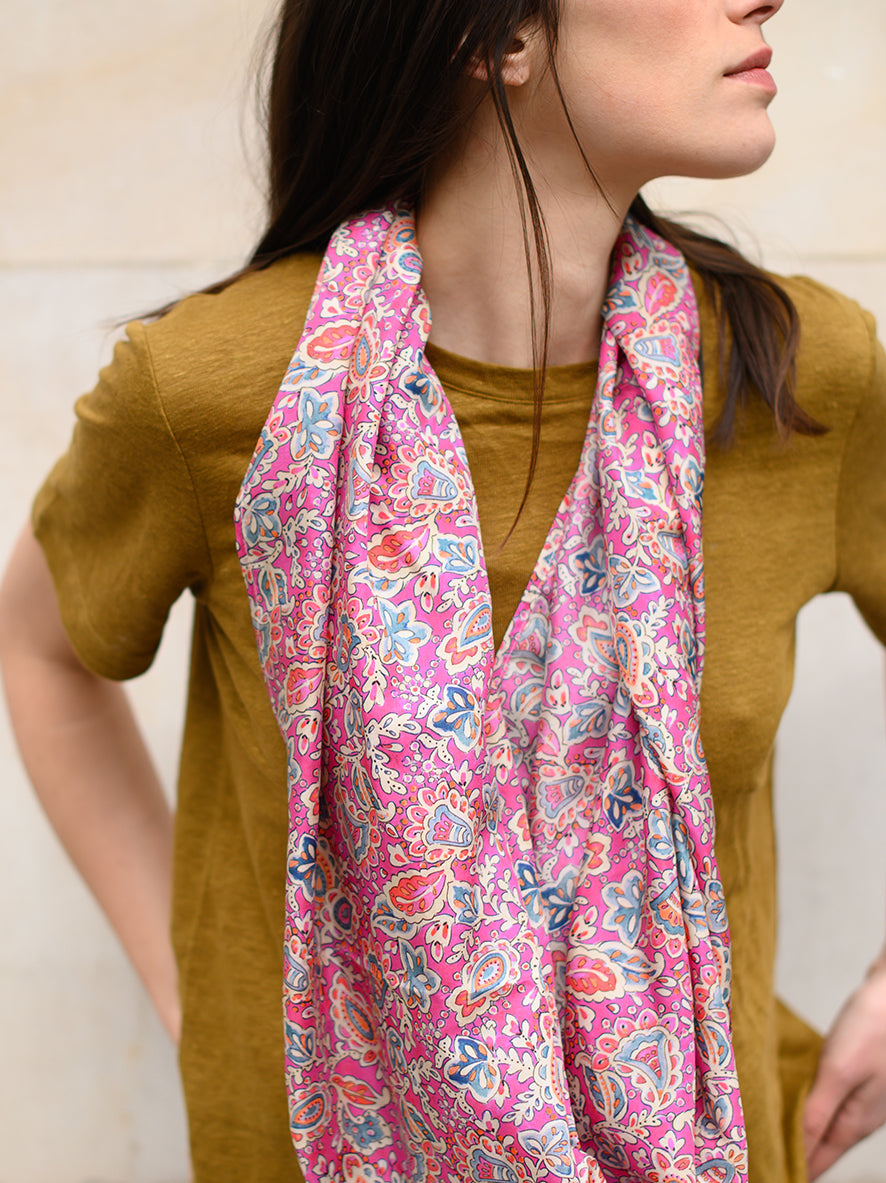 Foulard en soie 74 Meilleur Ami Paris, porté femme dénoué. Imprimé à cachemires colorés sur fond rose chatoyant.