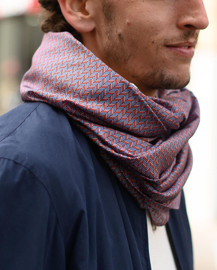 Foulard en soie 83 Meilleur Ami Paris, porté homme. Motifs graphiques dans les tons bleus, roses, rouges.