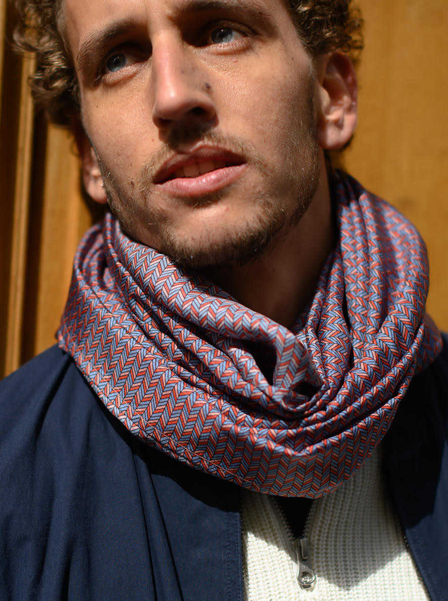 Foulard en soie 83 Meilleur Ami Paris, porté homme. Motifs graphiques dans les tons bleus, roses, rouges. Porté noué en 8 autour du cou.