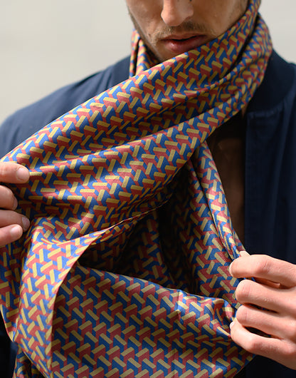 Foulard en soie 110 Meilleur Ami Paris, porté dénoué. Imprimé graphique effet 3D, coloris bordeaux, kaki et bleu.