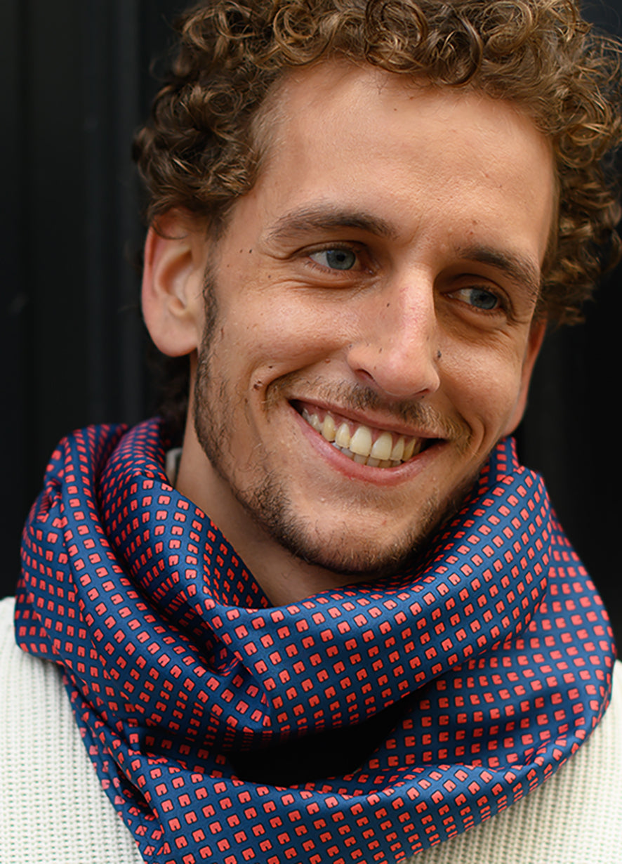 Foulard en soie 112 Meilleur Ami Paris, porté homme. Motifs rouge orangé sur fond bleu nuit.